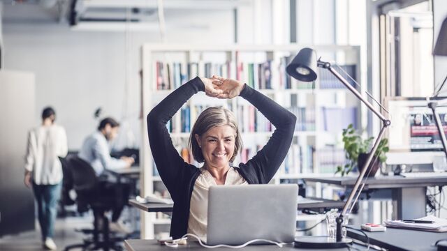 Smilende kvinne på kontoret foran datamaskinen sin.